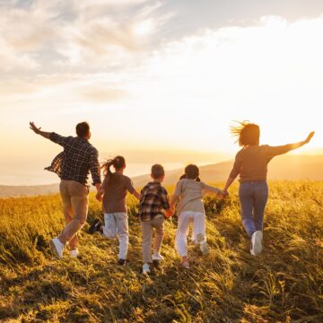 coperta foto cu o familie, parintii si 3 copii, alergand fericiti pe un camp
